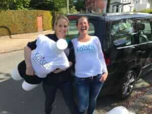 Daniela und Julia mit Musterpuppe und Kaiserschlüpfer-Shirt vor dem Auto auf dem Weg nach Kassel